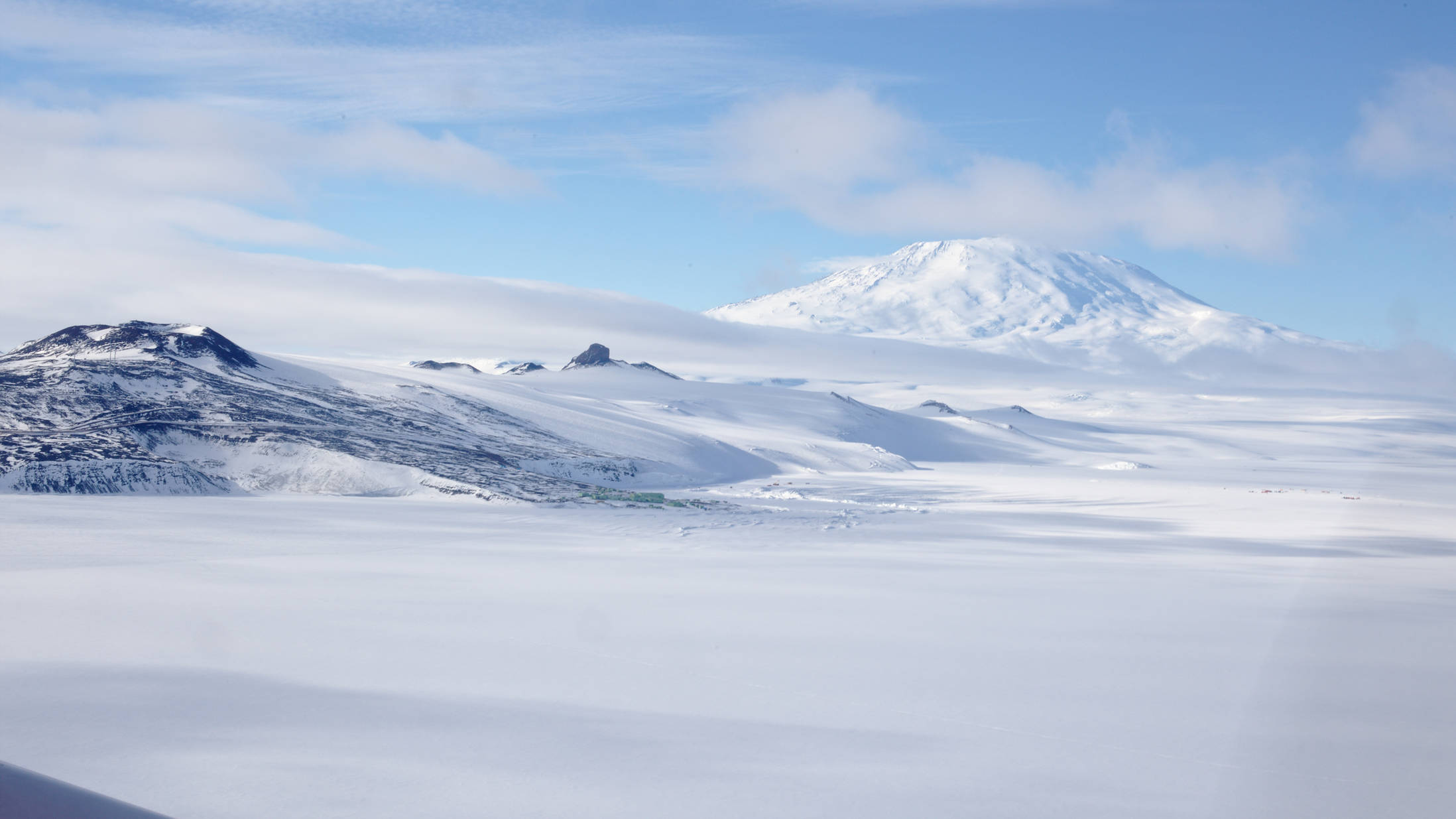 Ross Island. Dark sharp mountain in the centre: Castle Rock. In front of it the New Zealand station <em>Scott Base</em> Back right: Mount Erebus